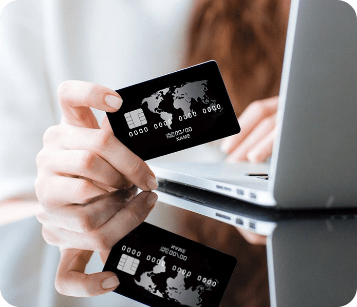 A person holding their credit card over the keyboard of a laptop.